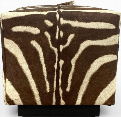 Pillowfina vintage zebra hide cube ottoman with natural brown and cream striped fur texture on a black base.
